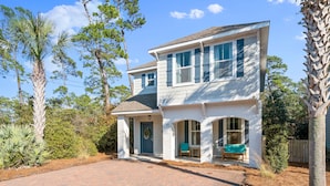 A two-story house with a covered porch, a brick driveway, and a variety of trees and shrubs in the yard.