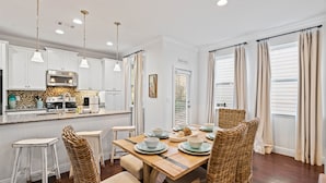A dining area with a wooden table, wicker chairs, and a kitchen in the background.