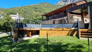 A wooden chalet with a balcony, surrounded by a grassy area and a mountain backdrop.