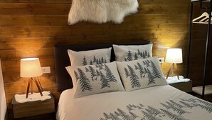 A bed with a white bedspread and pillows with tree designs, a wooden headboard, a fur throw, and bedside lamps.