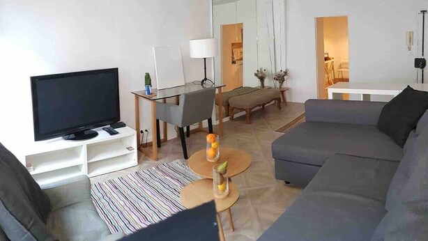 Una sala de estar moderna con un televisor de pantalla plana, un sofá gris y un comedor con mesa y sillas.