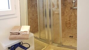 Un baño con cabina de ducha de vidrio, pared de ducha con azulejos y una pila de toallas sobre una superficie blanca.