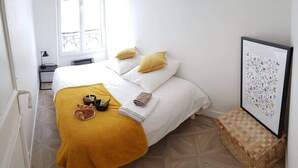 Una cama bien hecha con una manta amarilla, dos almohadas y un cuadro en la pared.