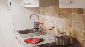 Una cocina compacta con gabinetes blancos, un lavamanos de acero inoxidable, un horno empotrado y una estufa a gas.