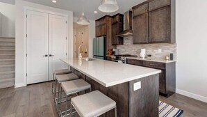 A modern kitchen with a large island, dark wooden cabinets, and pendant lighting.