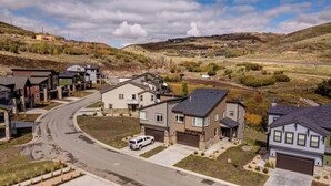 A residential area with houses, a winding road, and a hilly landscape in the background.