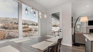 A modern dining area with a large table, chairs, and a view of a snowy landscape through large windows.