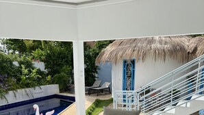Un espace aménagé au bord de la piscine, doté d’une structure à toit de chaume, de sièges extérieurs et d’un escalier menant à un niveau supérieur.