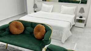 Une chambre moderne avec un grand lit, un canapé vert, un fauteuil vert et une petite table d’appoint avec une lampe.