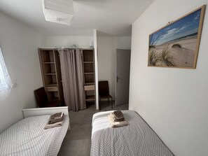 Une chambre avec deux lits simples, une armoire, une chaise et un tableau au mur.