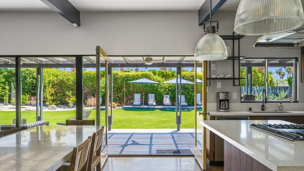 Cocina moderna con una isla grande, comedor con vistas al jardín y puerta de vidrio que da al exterior.