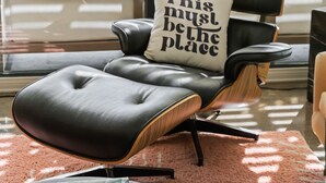Un área de estar exterior moderna con un sillón de cuero negro, un cojín blanco con texto y una lámpara colgante.