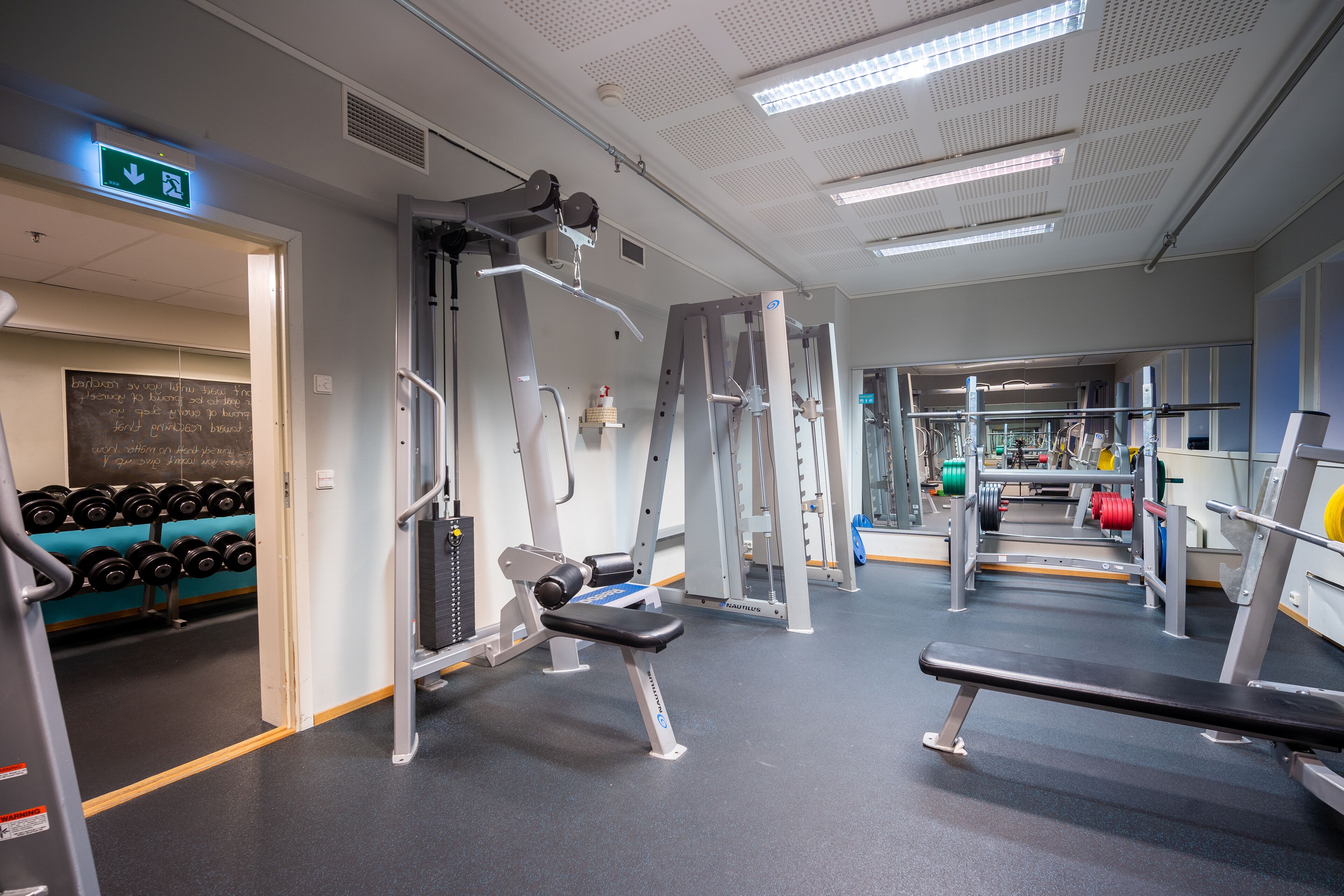 A gym with various exercise equipment, a bench, and dumbbells.