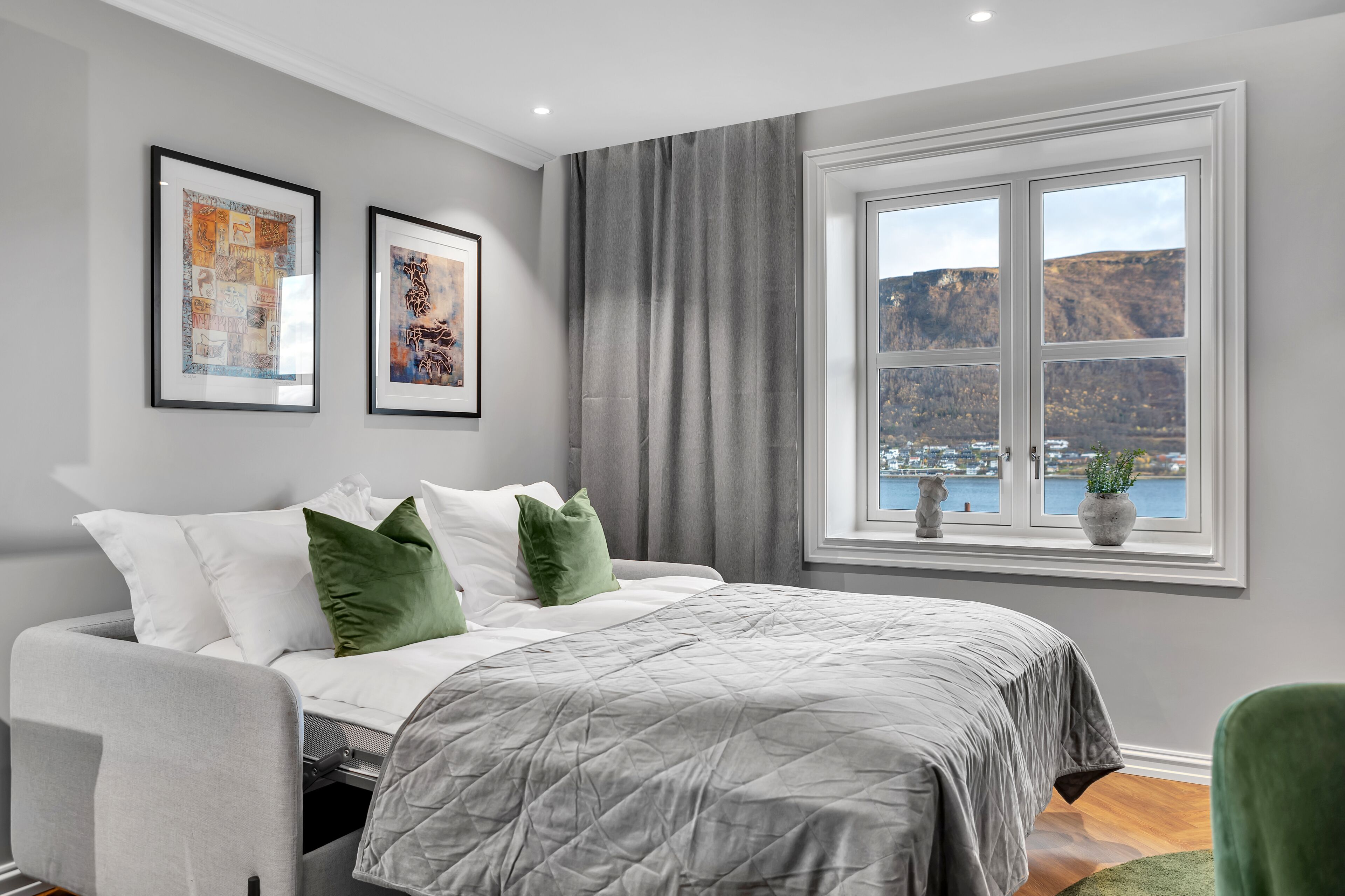 Un dormitorio moderno con una cama, vistas a un lago y montañas, y dos obras de arte enmarcadas en la pared.