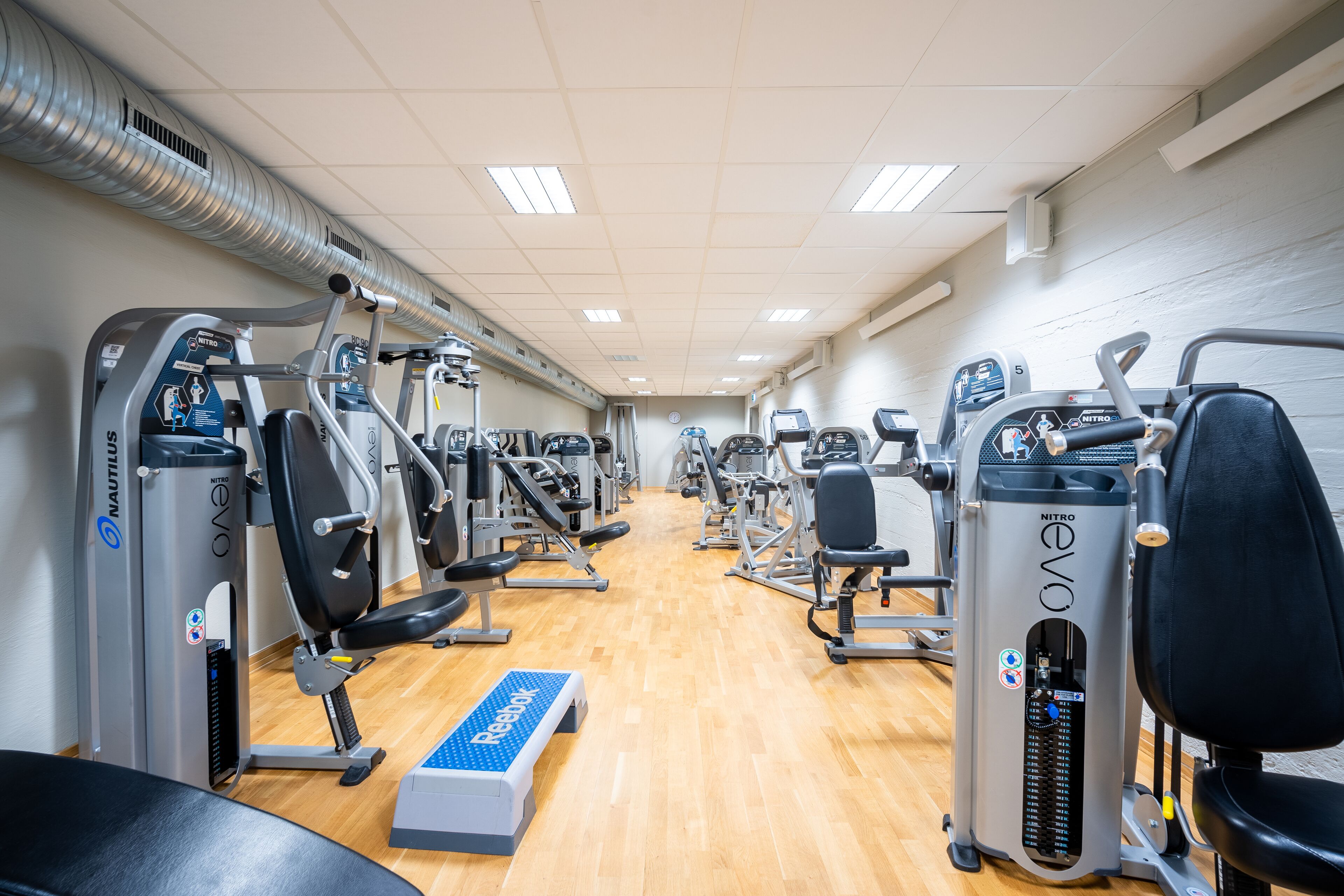 Ein Fitnessraum mit Nautilus- und Reebok-Geräten, einem Holzboden und einer Steigebene.