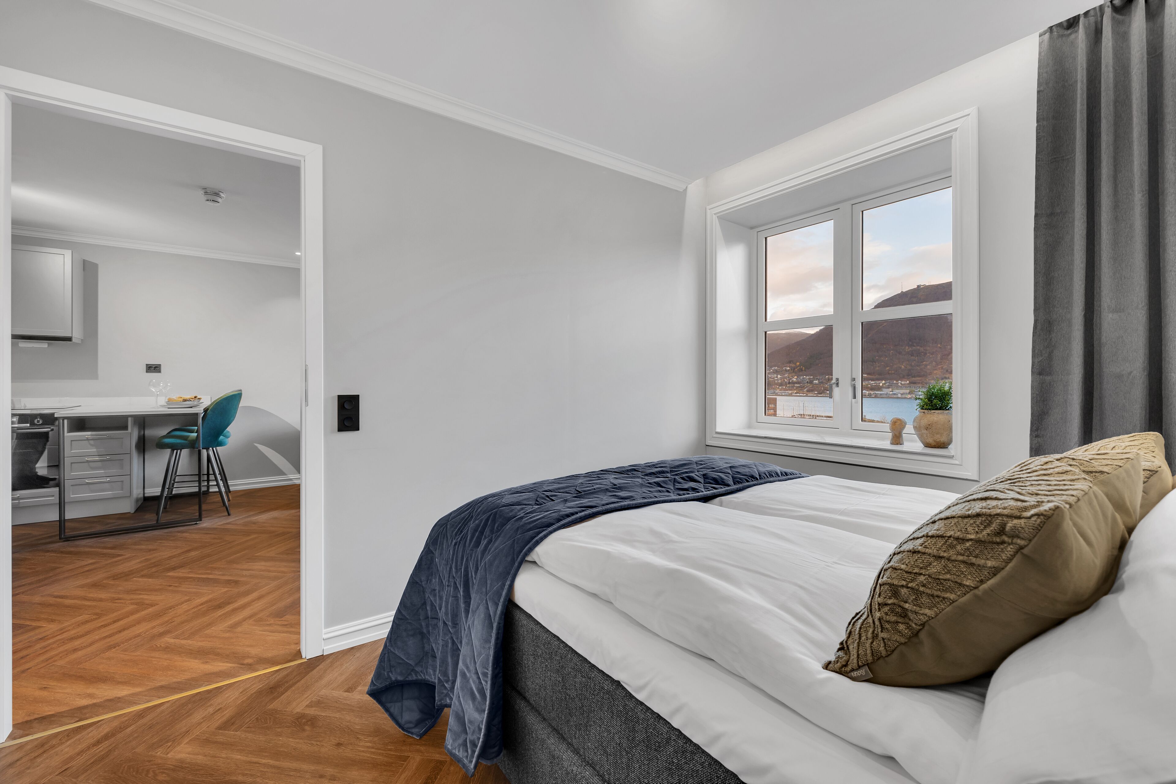 A bedroom with a bed, a window with a view, a desk, and a chair.