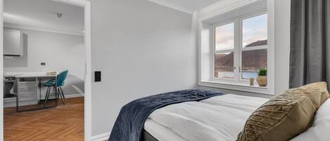 A bedroom with a bed, a window with a view, a desk, and a chair.