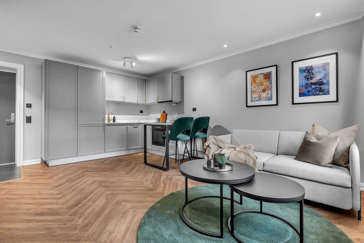 A modern living room with a grey sofa, two framed artworks, and a dining area with a table and chairs.