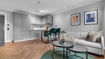 A modern living room with a grey sofa, two framed artworks, and a dining area with a table and chairs.