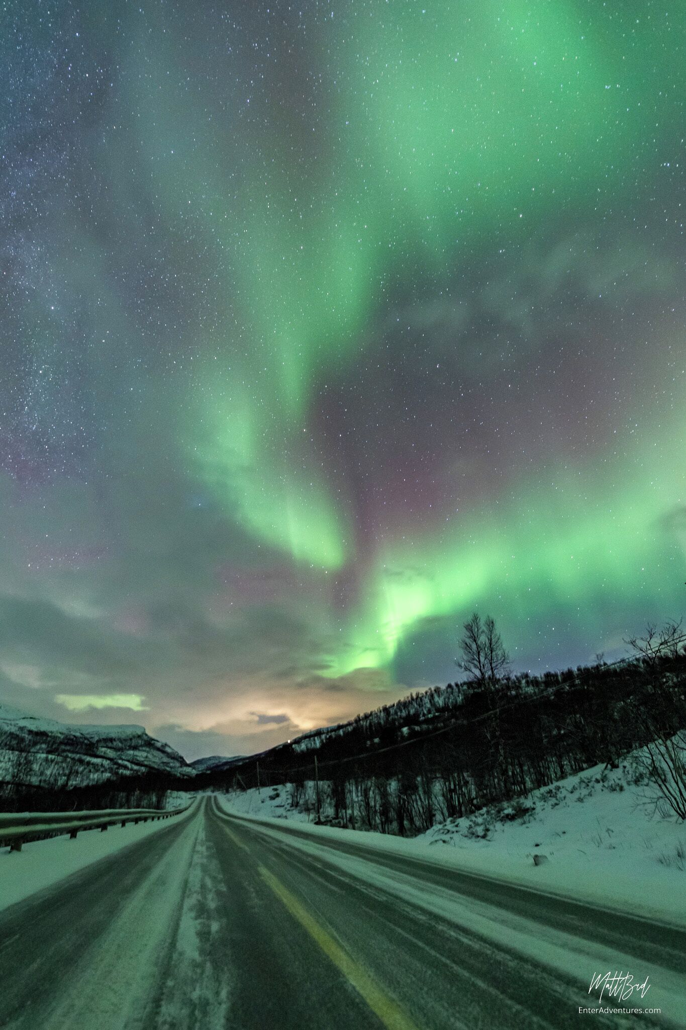 A road with snow-covered banks and a view of the northern lights.