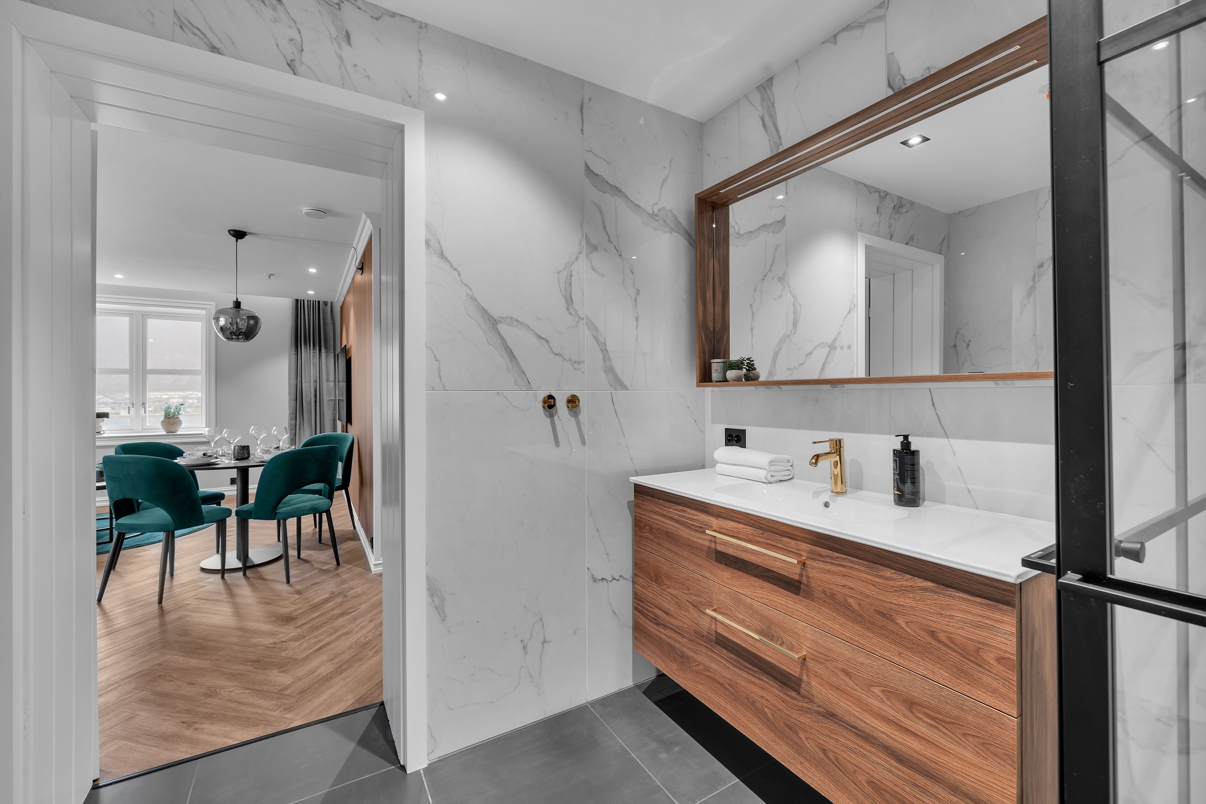 A modern bathroom with a marble wall, wooden vanity, and a large mirror.