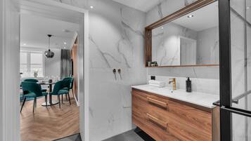 A modern bathroom with a marble wall, wooden vanity, and a large mirror.