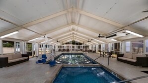 Una piscina interior con vista despejada al área de la piscina, incluyendo el borde, un espacio de descanso con asientos y un techo con luminarias.