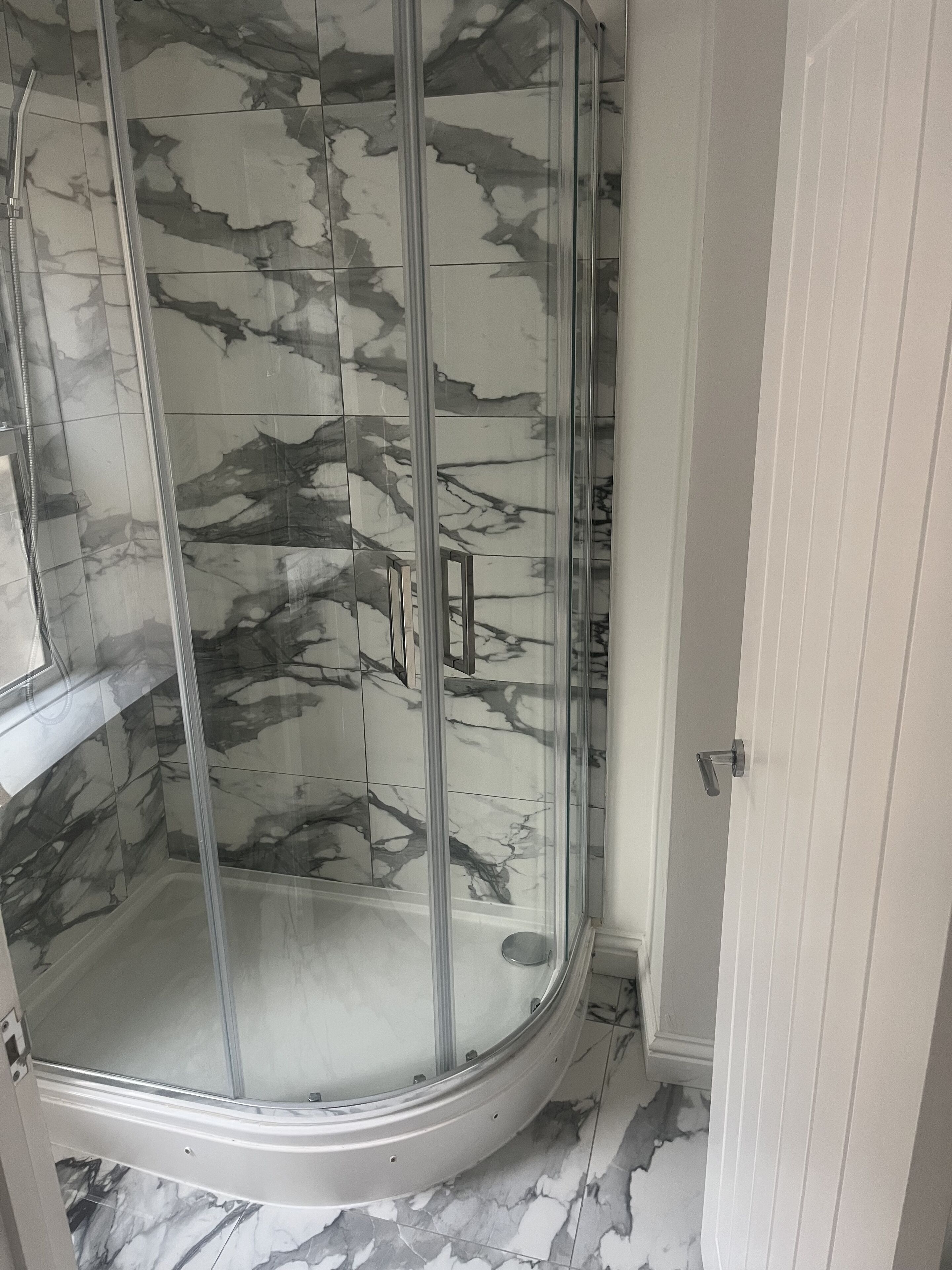 Une douche avec une porte en verre et des murs à motifs de marbre.