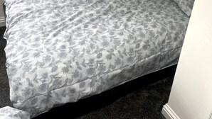 A single bed with a floral-patterned bedspread and pillows, a dark headboard, and a window on the left side. - Modern welsh cottage (penygraig)