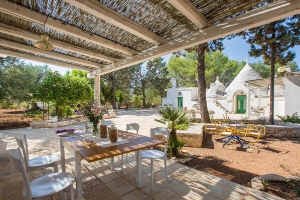 An outdoor patio with a table and chairs, surrounded by stone walls and greenery.