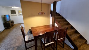 A dining area with a wooden table and chairs, a hanging light fixture, and a staircase with wooden steps. - Apartment Montfort (Feldkirch)