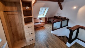A loft bedroom with exposed wooden beams, a built-in wooden wardrobe, a small desk, and a window providing natural light. - Apartment Montfort (Feldkirch)