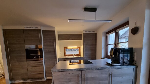 A modern kitchen with a central island, built-in appliances, and a window providing natural light. - Apartment Montfort (Feldkirch)