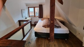 A bedroom with a wooden ceiling, a bed, a window with curtains, and a small table. - Apartment Montfort (Feldkirch)