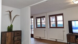 A spacious living room with a wooden cabinet, a television, and large windows offering a view of the outside. - Apartment Montfort (Feldkirch)
