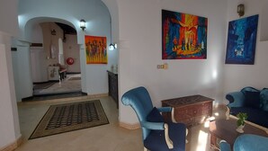 A living room with a blue sofa, a coffee table, and two blue armchairs. There are two paintings on the wall and a small wooden chest. - Horizon Palace (Zanzibar Town)