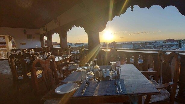A dining area with tables set for two, overlooking a cityscape during sunset. - Horizon Palace (Zanzibar Town)