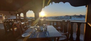 A dining area with tables set for two, overlooking a cityscape during sunset. - Horizon Palace (Zanzibar Town)