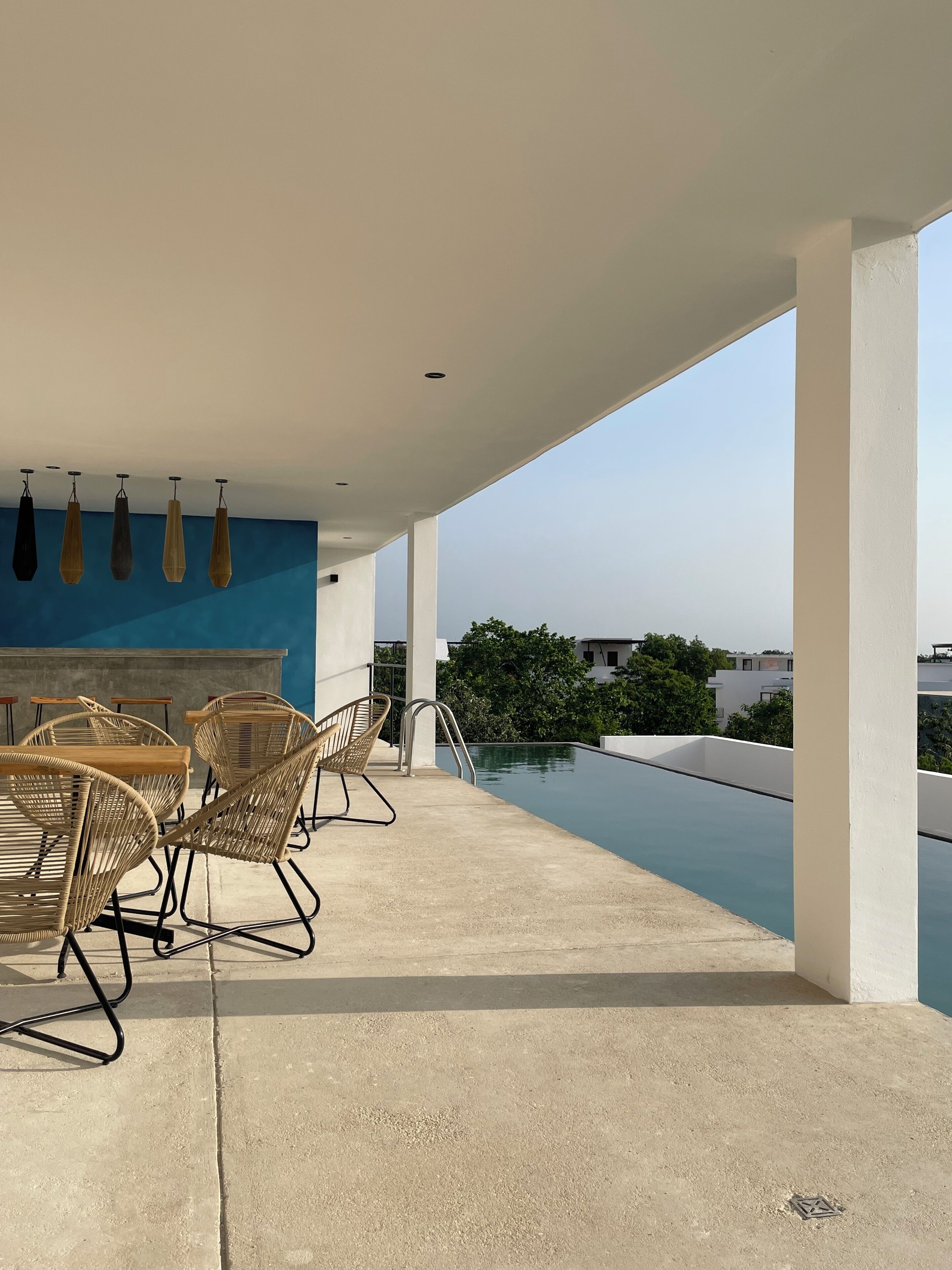Terraza en la azotea con piscina, sillas de descanso y una pared azul.