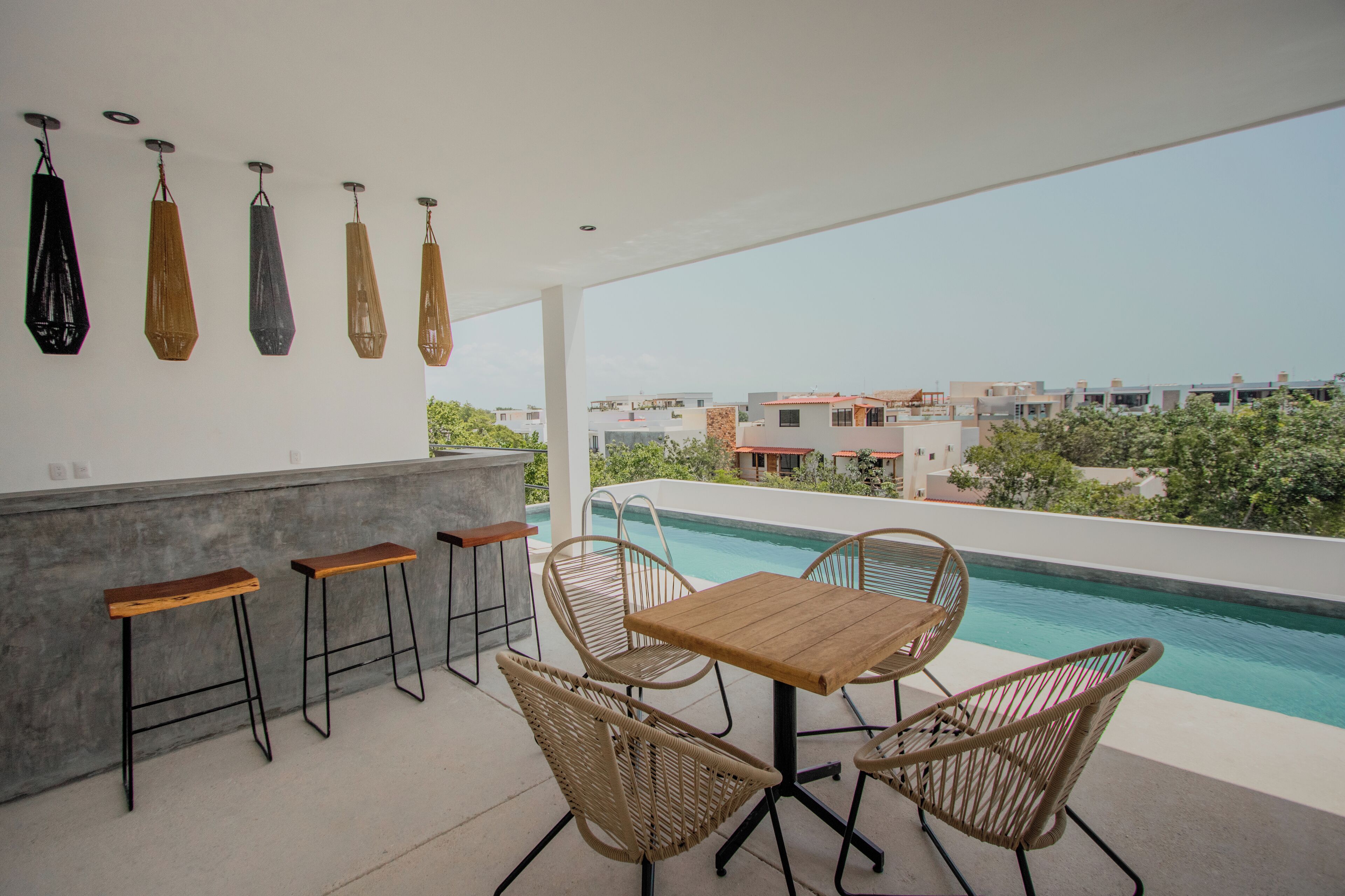 A patio with a pool, bar stools, wicker chairs, and hanging lights.