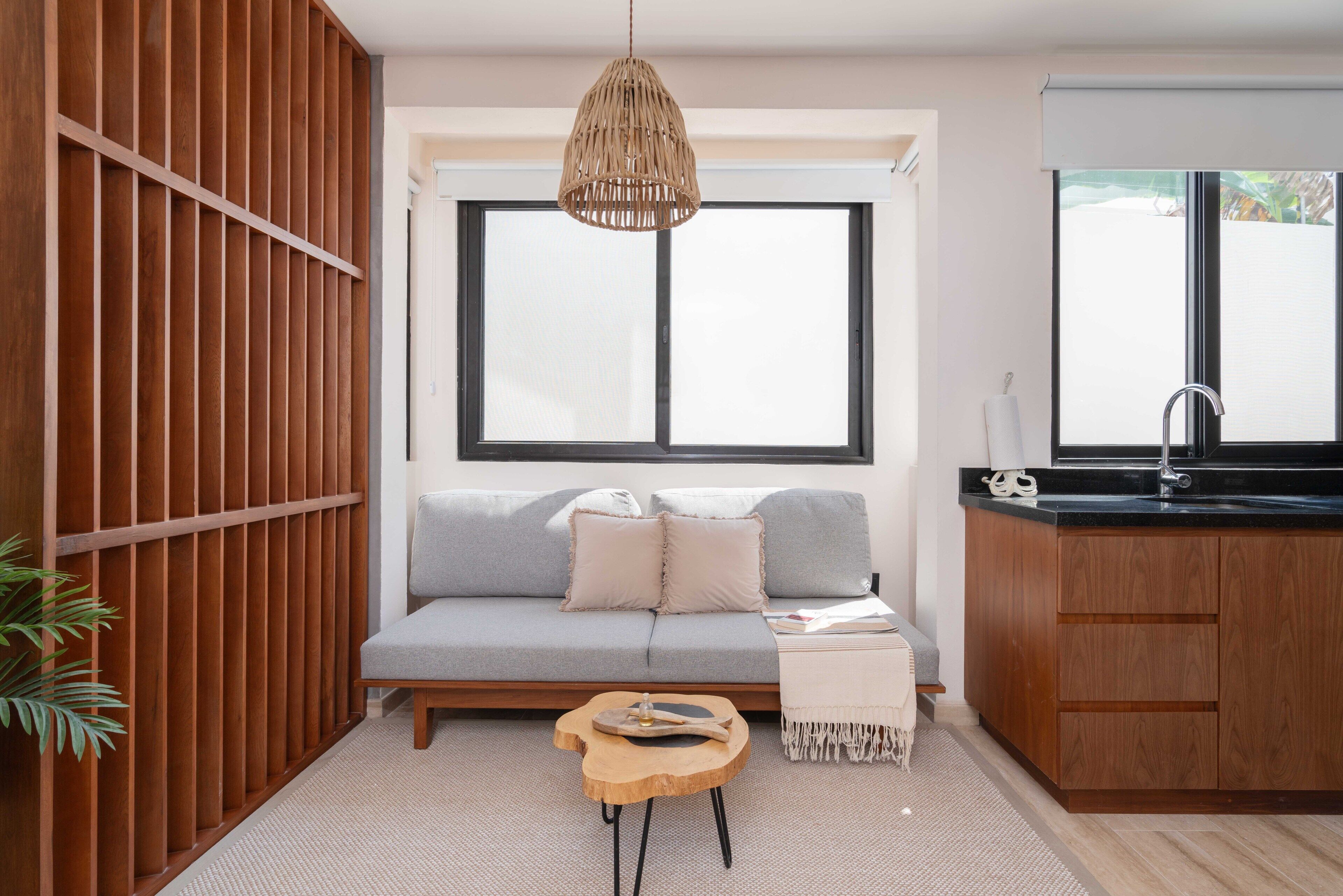 Una sala de estar moderna con un sofá gris, un panel de pared de madera y una cocina con encimera negra y lavabo.