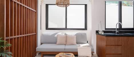 Un salon moderne avec un canapé gris, un mur recouvert de panneaux en bois et un coin cuisine doté d’un plan de travail et d’un évier noirs.