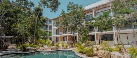 Un edificio moderno con piscina rodeada de plantas y árboles tropicales.