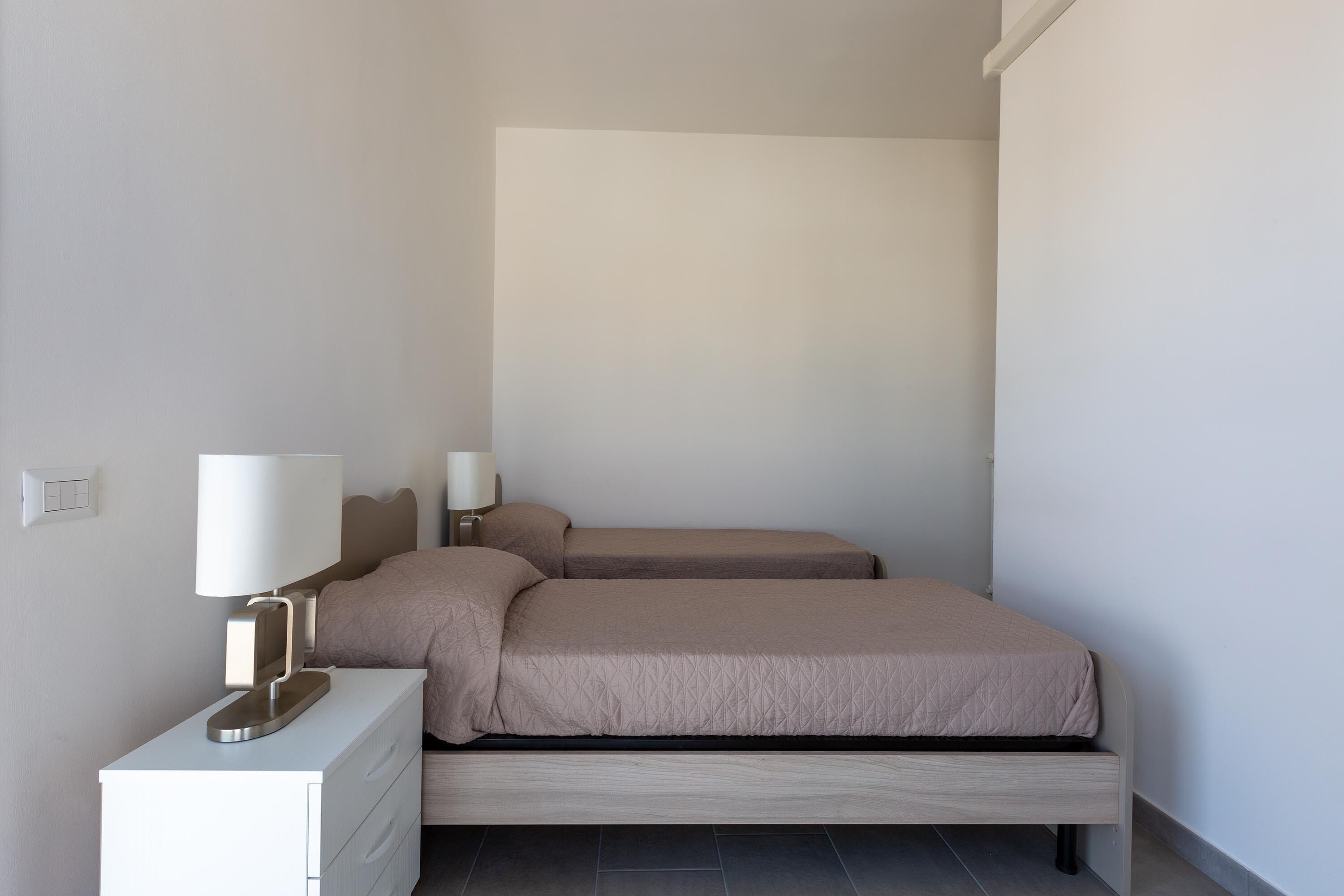 Ein Schlafzimmer mit zwei Betten, einem Nachttisch mit Lampe und einem Lichtschalter an der Wand.