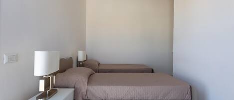 Ein Schlafzimmer mit zwei Betten, einem Nachttisch mit Lampe und einem Lichtschalter an der Wand.