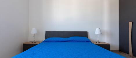 Un lit bien fait, avec une couverture bleue, deux lampes de chevet et une tête de lit sombre.