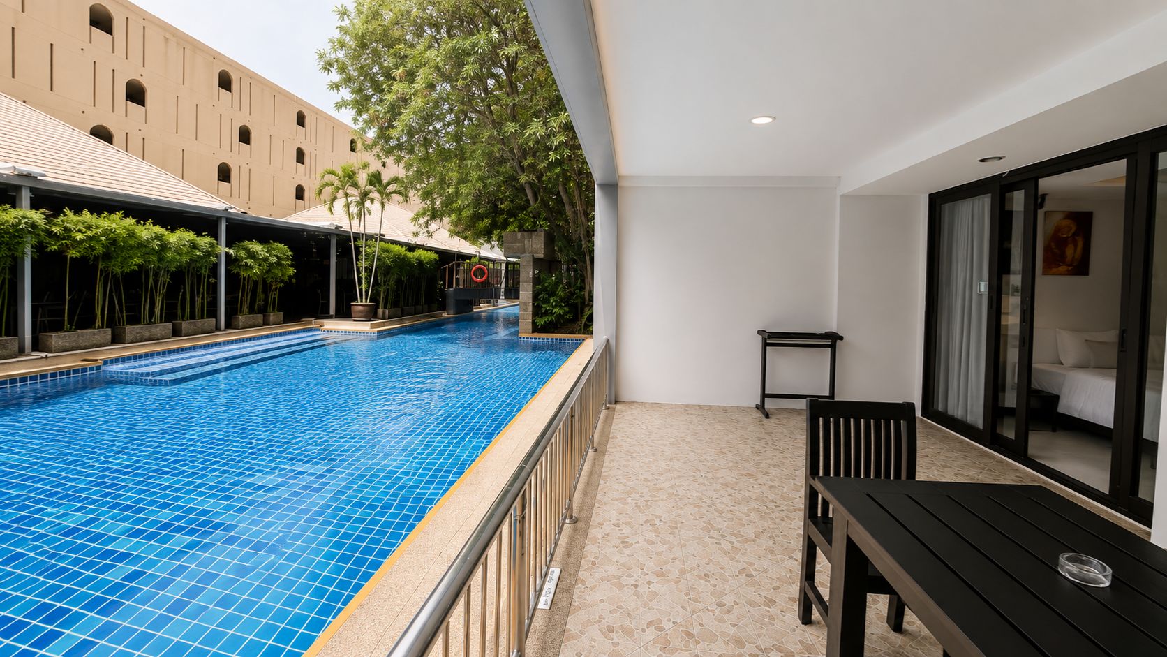 A swimming pool with a tiled floor, a small table and chair, and a building with arched windows in the background.
