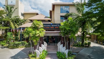 The entrance to Tuana Hotels Casa del Sol with a clear pathway, palm trees, and a modern building facade.