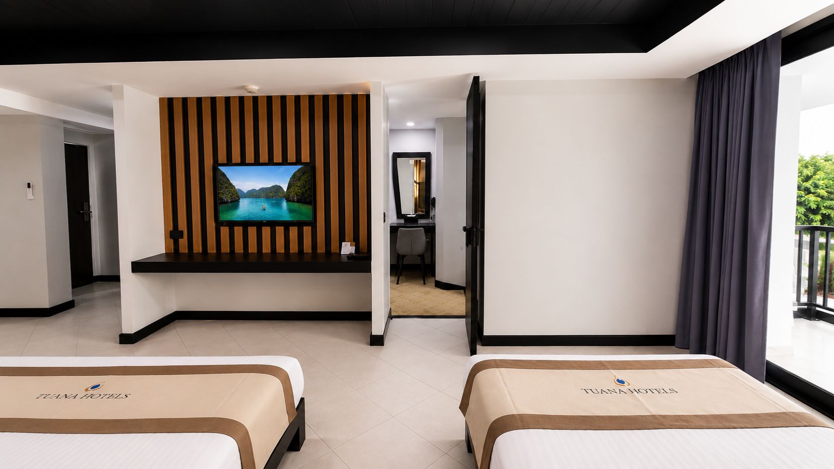 A hotel room with two beds, a TV on the wall, and a balcony with curtains.