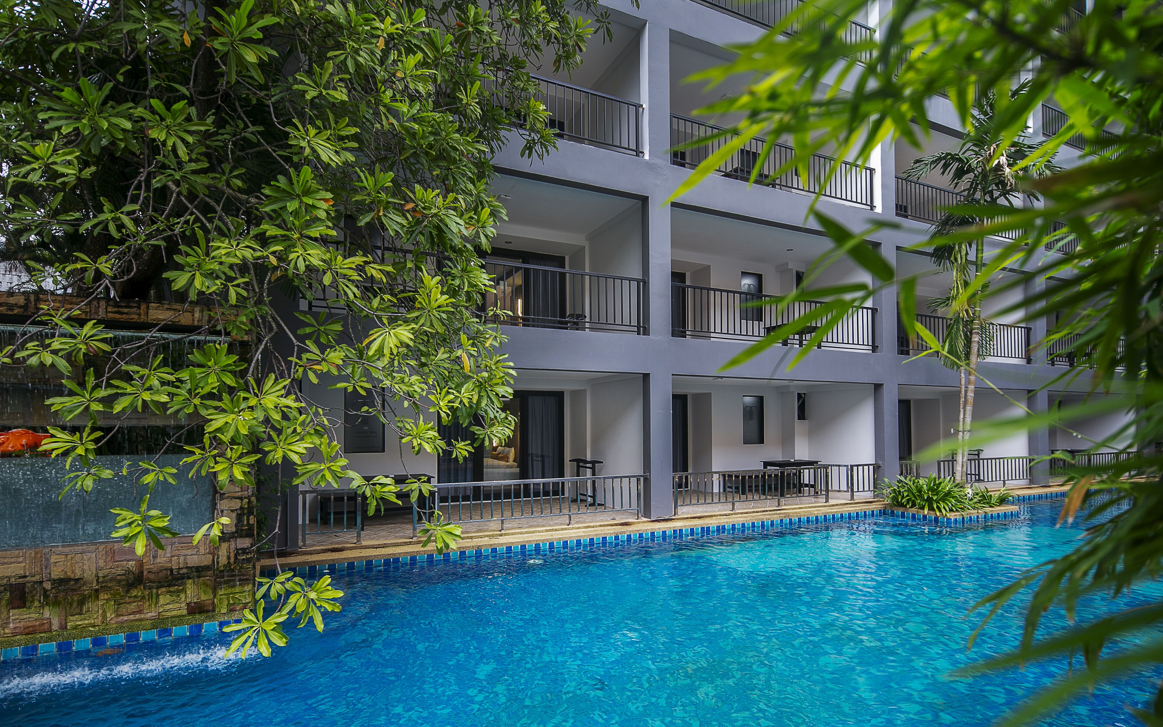 A multi-story hotel with a swimming pool surrounded by lush greenery.